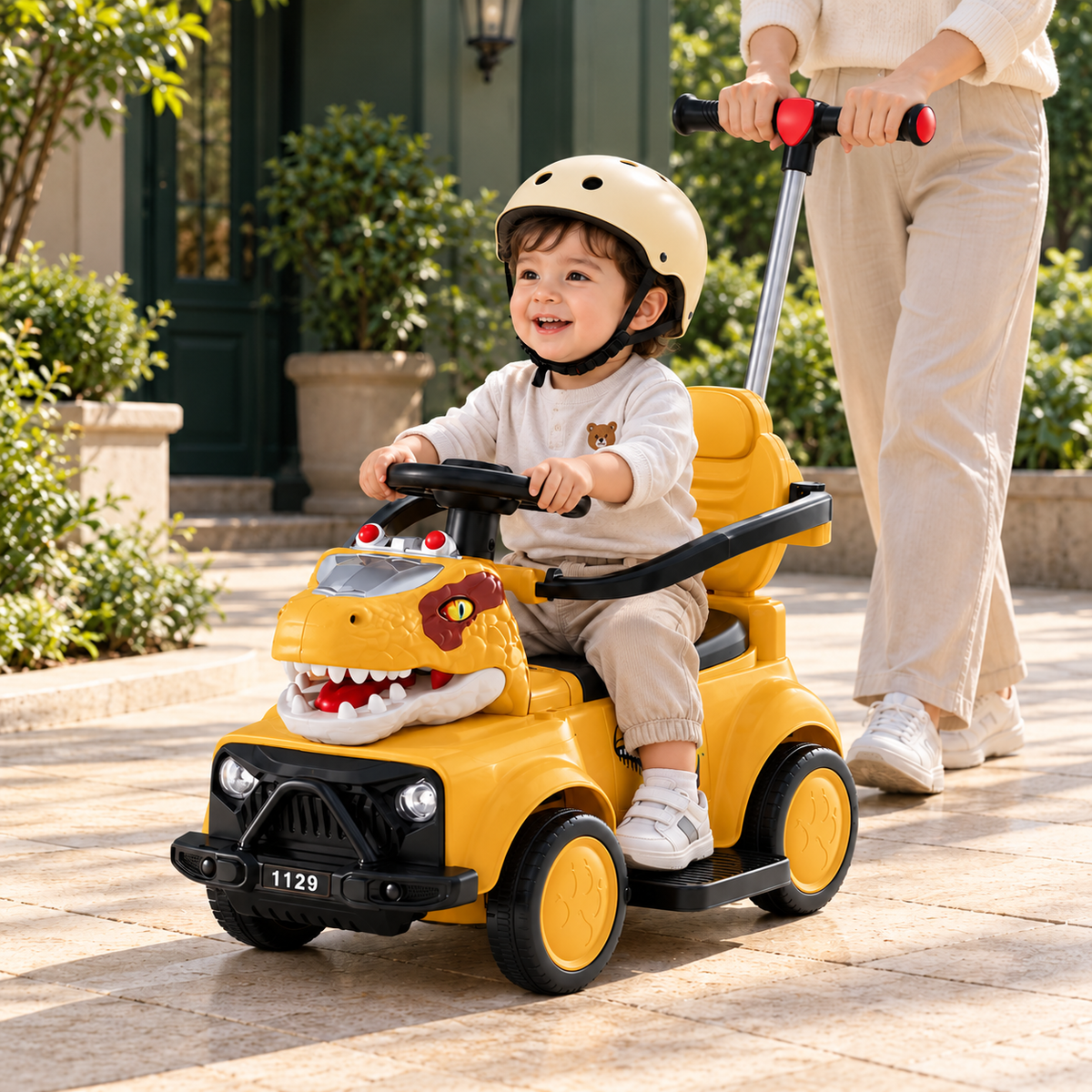 Niño sentado en el carro dinosaurio amarillo con casco y paseo acompañado por un adulto