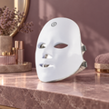 Máscara facial LED blanca con correas ajustables en un tocador cálido