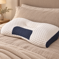Una almohada cervical blanca con panel azul oscuro sobre una cama de tonos cálidos